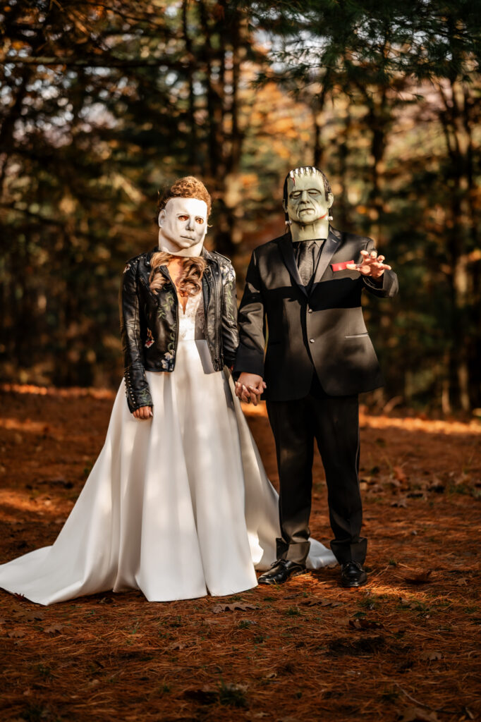 A couple has a fun halloween elopement in the adirondacks and are wearing halloween masks in the forest with the fall foliage.