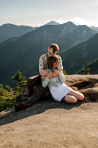 A couple hugs while sitting with adirondack mountains in the background.