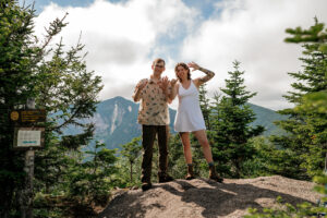 A couple shows the camera by holding up six fingers the number of high peak mountains in the adirondacks they have completed.