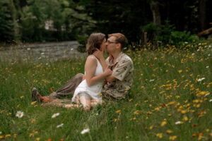 A couple kisses each other as they are sitting in a field of flowers on an Adirondack High peak HIke.