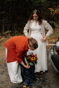 Two brides prepare for a hike by packing their flowers into their backpacks at the trailhead of Cobble Lookout in the Adirondacks.
