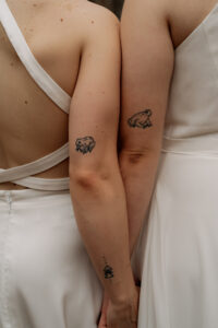 A photo of two brides and their matching frog tattoos on the back of their triceps.