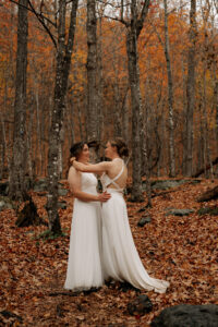 Two brides holding eachother in a Autumnal colored forest in the Adirondacks.