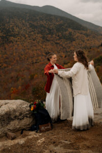 Two brides fold a picnic blanket and prepare to sit down and have hot cocoa.