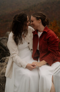 Two brides snuggled up on a mountain rock face in the fall.