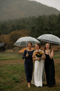 A bride walks with her family down the isle in the rain with clear umbrellas.