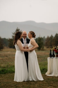 Two brides prepare to take their first kiss with a mountain backdrop in the rain.
