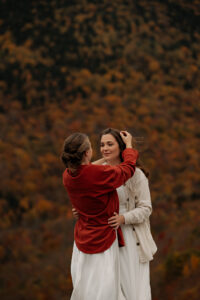 A bride moving the hair out of her wife's face with a mountain backdrop.